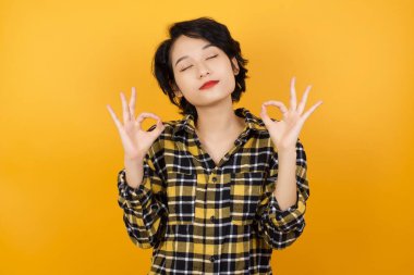 Gözleri kapalı gülümseyen genç bir kadın parmaklarıyla meditasyon hareketi yapıyor. Yoga konsepti.