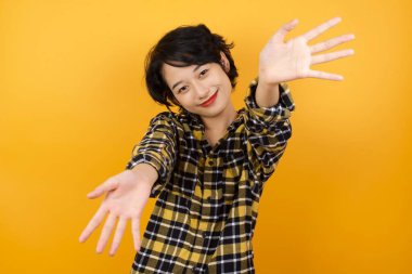 Güzel, genç bir kadın kameraya bakıyor. Sarılmak için kollarını açmış gülümsüyor. Mutluluğu kucaklayan neşeli bir ifade..