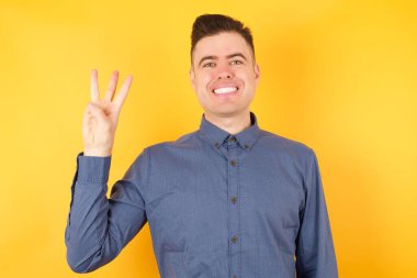 Yakışıklı genç işadamı kendini beğenmiş ve mutlu bir şekilde gülümserken üç numarayı işaret ediyor..