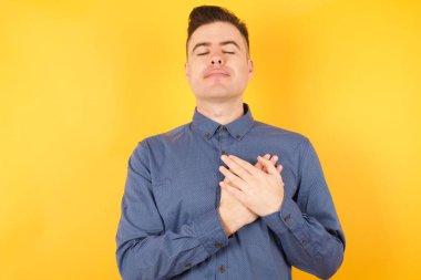 Yakışıklı genç işadamı elleri göğsünde gözleri kapalı gülümsüyor ve yüzünde minnet ifadesi var. Sağlık kavramı.