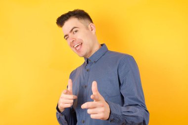 Yakışıklı genç işadamı kameraya mutlu bir şekilde göz kırpıyor ve parmaklarıyla işaret ediyor.  