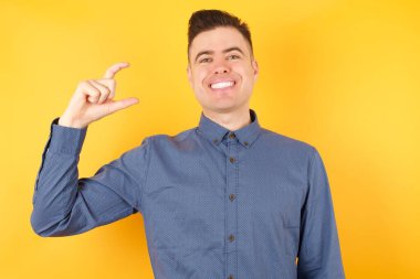 Yakışıklı genç iş adamı el hareketleriyle küçük boy işareti yapıyor, parmaklarına bakıyor ve kameraya bakıyor. Ölçü kavramı