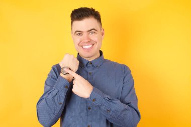 Kol saatini işaret eden yakışıklı genç işadamı, sabırsız, rahat bir ifadeyle kameraya bakıyor.