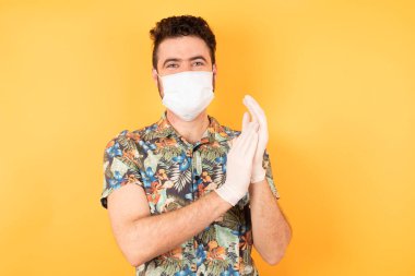 Koruyucu maskeli yakışıklı genç adam alkışlıyor ve mutlu, neşeli ve gururlu elleri bir arada..