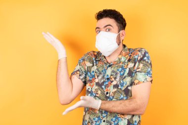 Koruyucu maskeli genç ve yakışıklı bir adam iki eliyle tuhaf bir şey gösteriyor.  