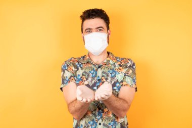 Koruyucu maskeli, genç ve yakışıklı bir adam ellerini birleştirip el kol hareketi yapıyor. Tutun ve koruyun