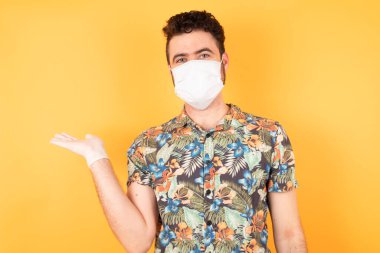 Koruyucu maskeli genç ve yakışıklı bir adam sunuyorum ve avuç içi kameraya bakıyorum..