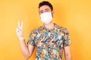 Koruyucu maskeli genç yakışıklı zafer işareti yapıyor. İki numara..