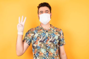 Koruyucu maskeli genç yakışıklı üç numaralı parmaklarıyla onu gösteriyor ve işaret ediyor.  