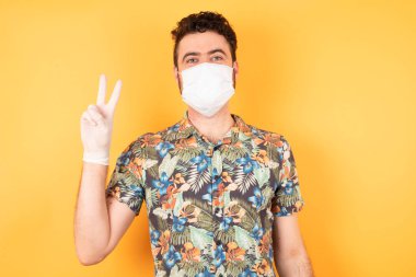 Koruyucu maskeli genç yakışıklı iki numaralı parmaklarıyla onu işaret ediyor.  