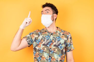 Koruyucu maskeli genç ve yakışıklı bir adam başarılı bir fikri işaret ediyor. Heyecanlı ve mutlu. Bir numara..