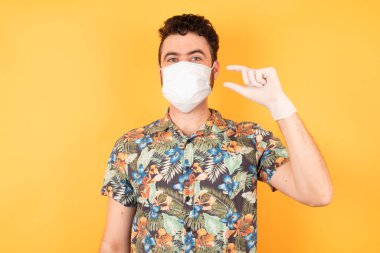 Koruyucu maskeli yakışıklı, gülümseyen, kendine güvenen, el hareketi yapan, parmaklarıyla işaret yapan ve kameraya bakan genç bir adam. Ölçü kavramı