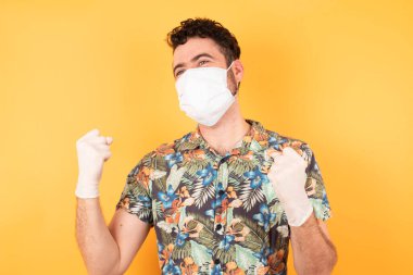 Koruyucu maskeli yakışıklı genç adam kolları havada ve gözleri kapalı bir şekilde başarının şaşkınlığı ve şaşkınlığı içindeydi. Kazanan konsept.