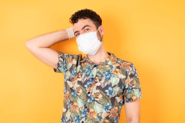 Koruyucu maskeli yakışıklı bir genç kafası karışmış ve bir şeyi merak ediyor. Elini başının üstünde tutuyor, şüpheyle emin değil. Düşünceli kavram.