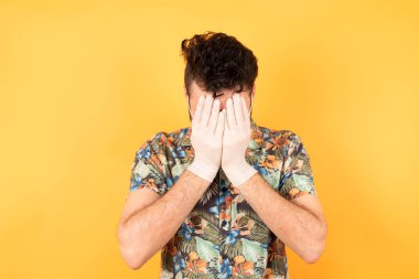 Elleriyle yüzünü kapatan koruyucu maskeli yakışıklı genç adam yıkılmış ve ağlıyor..