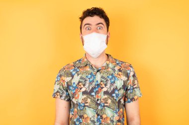 Sarı stüdyodaki tıbbi maskeli, korkmuş beyaz adam, covid ve corona virüsü. 