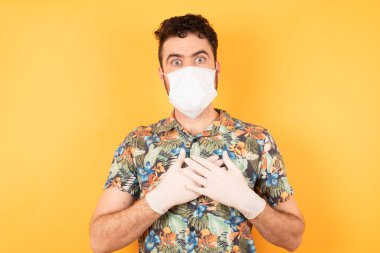 Sarı stüdyodaki tıbbi maskeli, korkmuş beyaz adam, covid ve corona virüsü. 