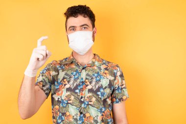 Sarı stüdyoda tıbbi maskeli beyaz bir adam, işaret ediyor. 