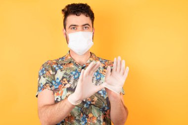 Sarı stüdyodaki tıbbi maskeli, korkmuş beyaz adam, covid ve corona virüsü. 