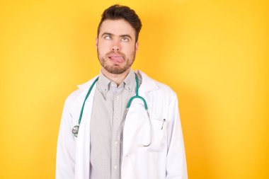 Genç, yakışıklı doktor adam, yüzünü ekşiterek gözlerini kesiyor ve sarı arka planda izole edilmiş bir dil gösteriyor. Komik ve çılgın olmak