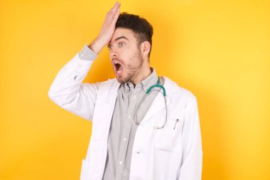 Sarı arka plan üzerinde tıbbi üniforma giyen yakışıklı, beyaz bir doktor. Hatayla el ele tutuşurken şaşırmış. Hatayı hatırla. Unuttum, kötü hafıza konsepti.