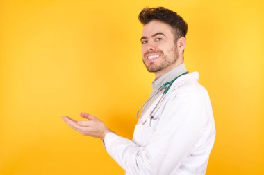 Tıp üniforması giyen yakışıklı beyaz doktor avuçlarını açık tutuyor. 