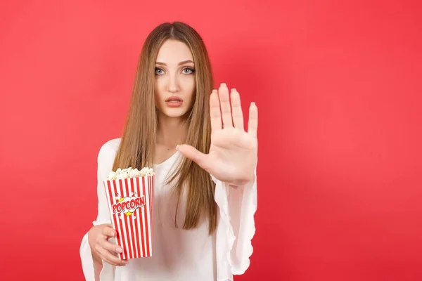 Young beautiful woman with popcorn doing stop gesture with palm of the hand. Warning expression with negative and serious gesture on the face