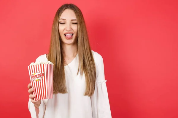 Young beautiful woman with popcorn sticking tongue out happy with funny expression. Emotion concept.