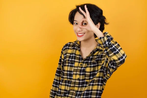 beautiful young woman  doing ok gesture with hand smiling, eye looking through fingers with happy face.