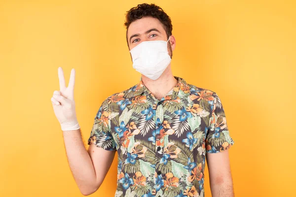 Koruyucu maskeli genç yakışıklı zafer işareti yapıyor. İki numara..