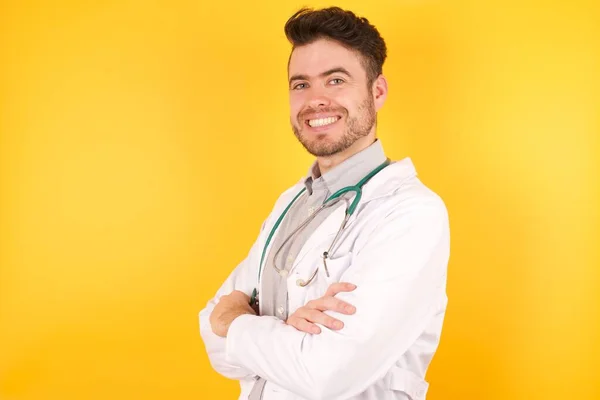 年轻的白人医生 身穿制服 身披黄底 双手交叉地微笑着 望着摄像机 积极的人 — 图库照片