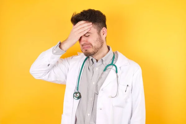 A very upset and lonely doctor man wearing medical uniform crying, standing against a wall.