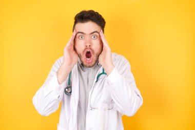 Korkak suratlı, elleri başının üstünde, çenesi düşmüş, tıbbi üniforma giymiş, sarı arka planda duran duygusal doktor. Omg kavramı