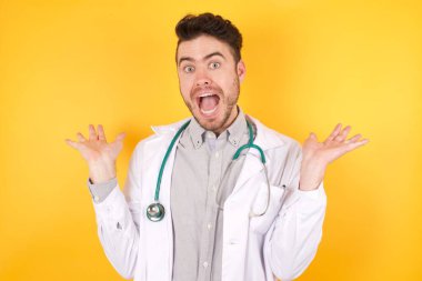 Tıp üniforması giyen yakışıklı, beyaz bir doktor çılgın ve başarıyı kollarını kaldırıp heyecanla haykırarak kutluyor. Kazanan konsept