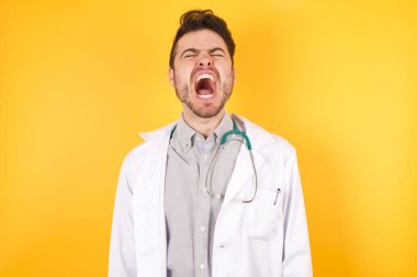 Genç, yakışıklı, beyaz doktor üniformalı kızgın ve kızgın çığlıklar atan öfkeli, öfkeyle bağıran bir adam. Öfke ve agresif kavram.