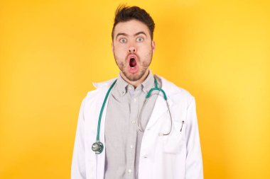 - Aman Tanrım! Şaşkın doktor üniforması giyiyor, şok olmuş bir ifadeyle kameraya bakıyor, beklenmeyen bir şekilde bağırıyor, sarı arka planda izole edilmiş.