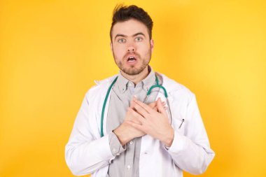 Tıbbi üniforma giyen korkmuş Avrupalı doktor, korkmuş bir ifadeyle bakıyor, ellerini göğsünde tutuyor, beyaz arka planda izole edilmiş garip bir şeyi fark etmek için kafası karışıyor. Millet, sessiz tepki ve duygular..