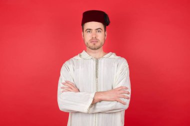 Fez takan yakışıklı genç adamın portresi havalı ve kendinden emin bir girişimcinin beyaz üzerine izole edilmiş kırmızı gömlek giydiğini hissediyor..