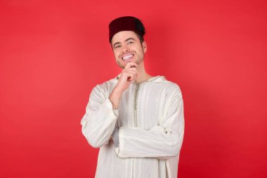 Geleneksel Türk şapkası giyen yakışıklı genç adam Fez ellerini kısmen çapraz tutuyor ve ellerini çenesinin altında tutuyor, kameraya zevkle bakıyor. Mutlu duygu konsepti.