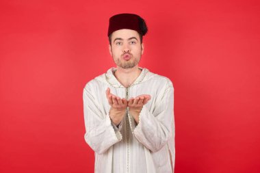 Geleneksel Türk şapkası giyen yakışıklı genç adam Fez dudak bükerek öpücük yolluyor ve hava öpücüğü vermek için avuç içi tutuyor..