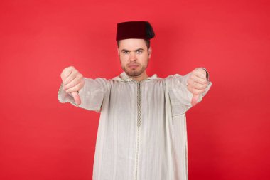 Geleneksel Türk şapkası giyen yakışıklı genç adam Fez iki parmağını aşağıda tutarak üzgün. Konseptten nefret. 