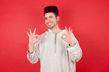 Sakin ol, her şey mükemmel. Geleneksel Türk şapkası giyen mutlu ve keyifli genç adamın portresi tamam jest yapıyor ve gülümsüyor..