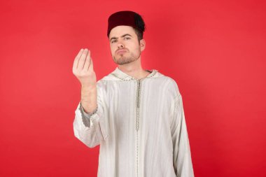What the hell are you talking about. Shot of frustrated handsome young man wearing fez gesturing with raised hand doing Italian gesture, frowning, being displeased and confused with dumb question.