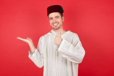 Genç, yakışıklı, fes takan, el ve baş parmağını kaldıran, mutlu ve neşeli gülümseyen genç bir adam..