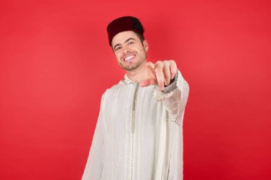 Fes takan yakışıklı genç adam kameraya bakıyor. Tatmin olmuş, kendinden emin, dostane bir gülümsemeyle. Düz renkli duvara karşı seni seçiyor.