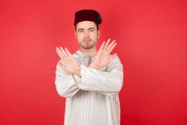 Fes takan yakışıklı genç adam reddedilmiş. Kollarını kavuşturmuş, avuç içleri negatif işareti yapıyor. Kızgın surat..
