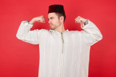 Fes takan yakışıklı genç adam gururla gülümseyen kol kaslarını gösteriyor. Fitness konsepti.