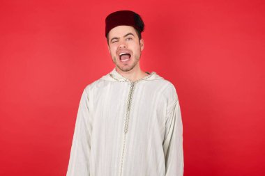 Fes takan yakışıklı genç adam kameraya seksi bir ifadeyle bakıyor, neşeli ve mutlu bir yüzle..