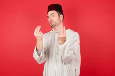 Kırmızı arka planda poz veren fes takan yakışıklı bir genç.