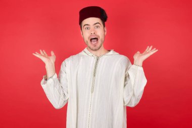 Kırmızı arka planda poz veren fes takan yakışıklı bir genç.